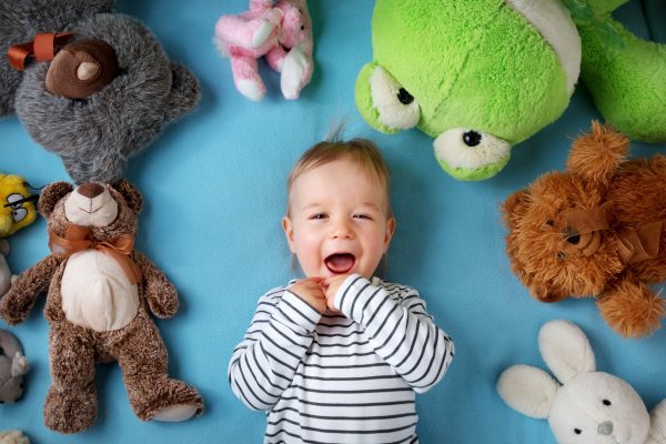 Happy one year old boy lying with many plush toys on blue blanket